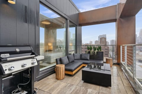 Modern balcony with a sectional sofa, grill, and skyline view.