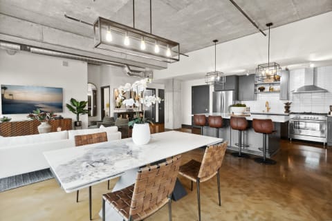 A contemporary dining and living area with a marble table, leather chairs, and exposed concrete ceiling.