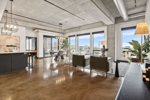 A modern living room with concrete walls, polished floors, and large windows overlooking the city.