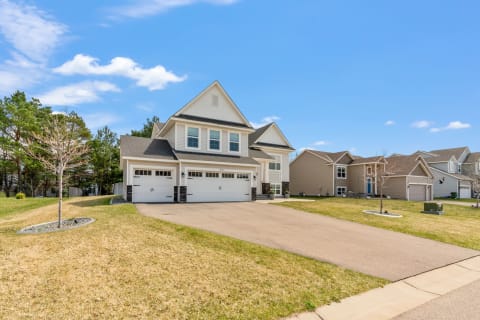 A modern two-story house with a double garage, surrounded by green grass and a blue sky.