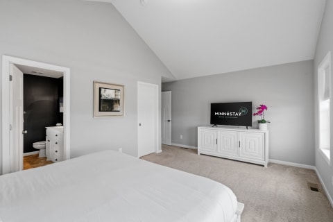 Spacious bedroom with white bedding, a TV, and a bathroom door.