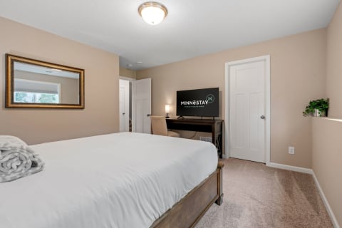 Cozy bedroom with a made bed, desk, and flat-screen TV.