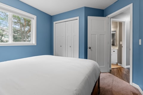 Interior view of a bedroom featuring a white bedspread, blue walls, and a doorway to a bathroom.