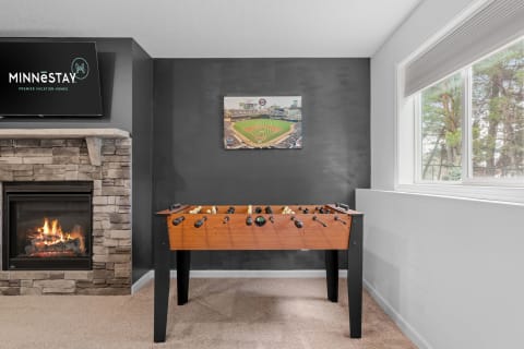 A spacious leisure room featuring a foosball table, a fireplace, and a television.