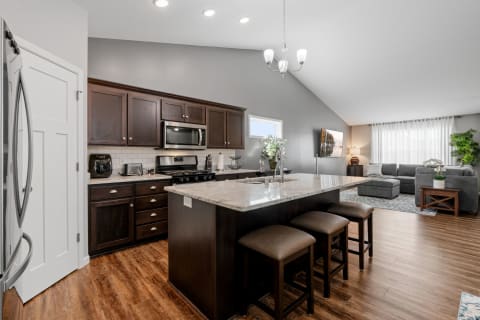 Modern kitchen with dark wood cabinets and granite countertops connected to a living room.