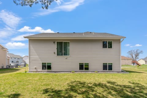 Back view of a light-colored home with windows and a green lawn under a blue sky.
