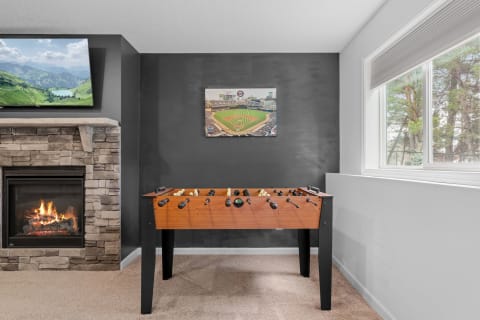 A room featuring a foosball table, stone fireplace, and a mounted television with a landscape image.
