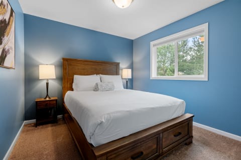 A cozy bedroom featuring a wooden bed, blue walls, and a window with a view.