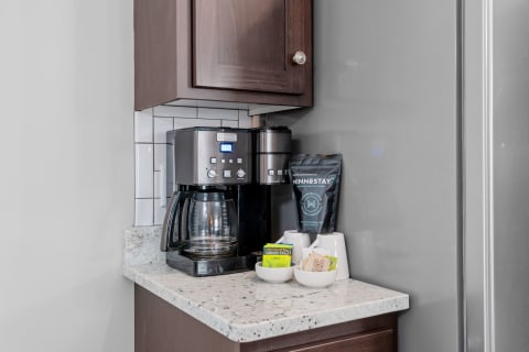 A coffee maker on a granite countertop with tea packets and a bag labeled 'MINNSTAY'.