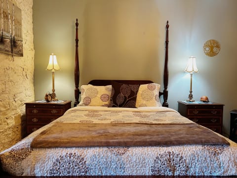 A stylish bedroom featuring a four-poster bed, nightstands with lamps, and a textured stone wall.
