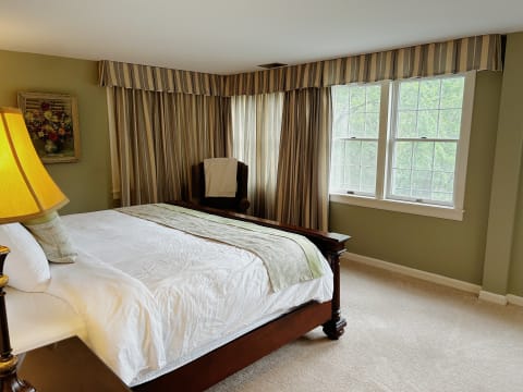 An elegant bedroom featuring a dark wooden bed, warm lighting, and large windows with scenic views.
