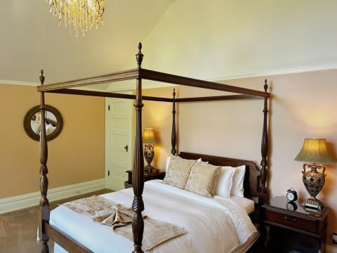 An elegant bedroom with a four-poster bed, ornate chandelier, and decorative lamps creating a warm ambiance.