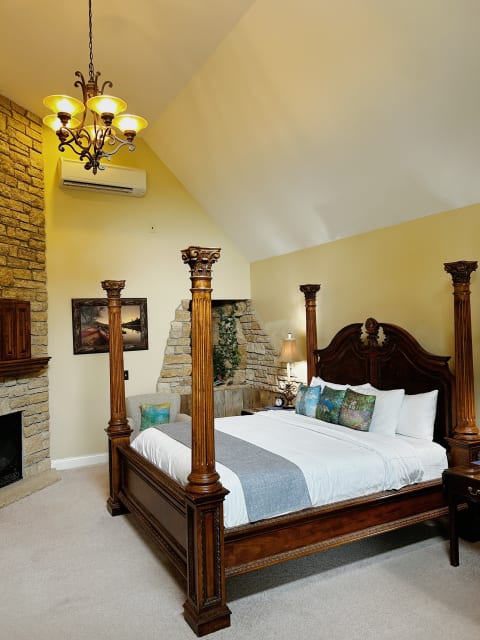 A luxurious bedroom with a four-poster bed, stone fireplace, and elegant chandelier.