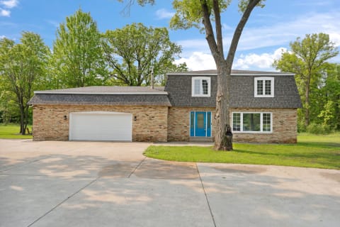 Two-story house with blue doors and surrounded by trees.