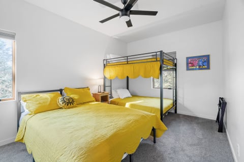 Bright bedroom with a bunk bed and a single bed, decorated in yellow, featuring a piece of colorful artwork on the wall.