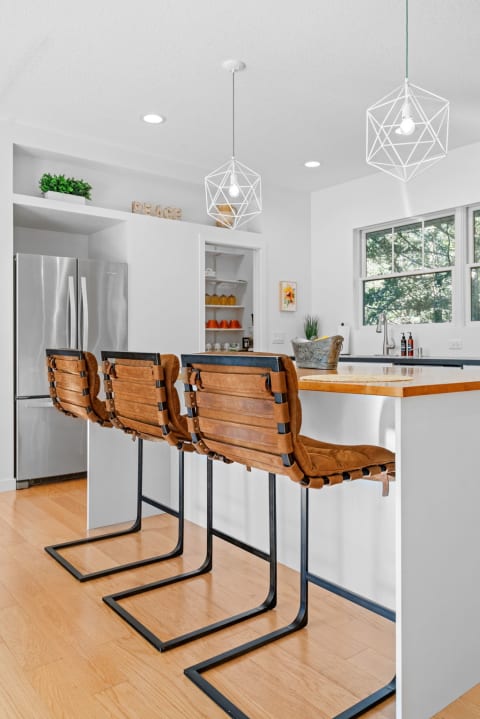 A bright kitchen with leather bar stools and geometric lighting.