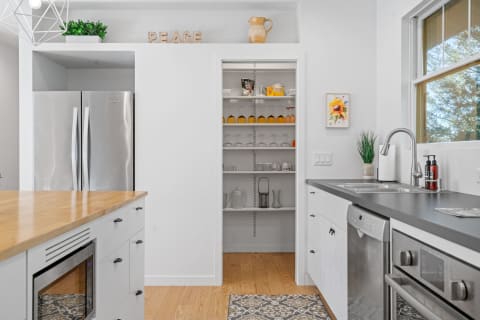 A sleek kitchen with stainless steel appliances, an organized pantry, and a wooden countertop.