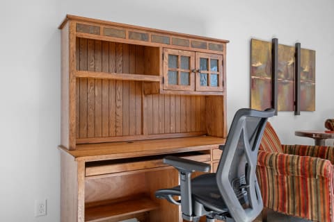 Wooden desk hutch with glass panel doors and ergonomic chair, featuring abstract art on wall.