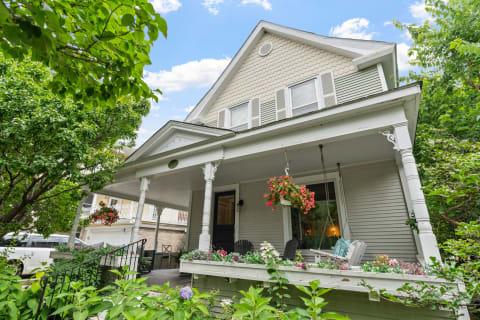 A two-story house with a porch adorned with flowers and surrounded by greenery.