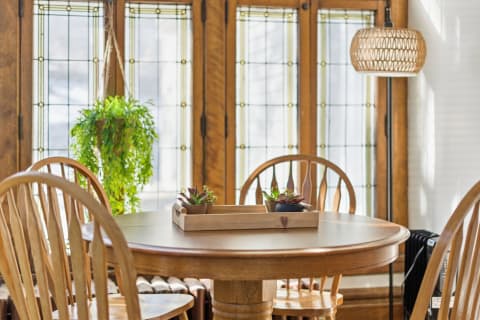 A round wooden dining table with succulent plants in a sunny room with decorative windows and a hanging light.