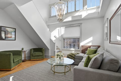 A bright living room with green furniture, a glass coffee table, and large windows letting in sunlight.