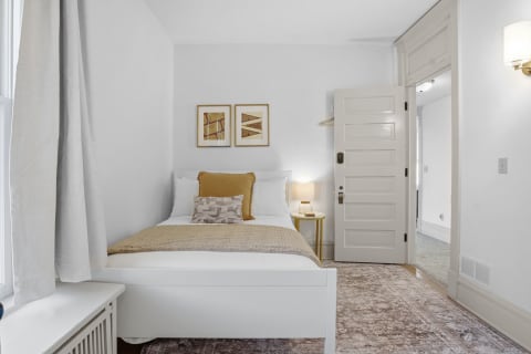 A minimalistic bedroom with a white bed, textured golden blanket, and warm decor accents.