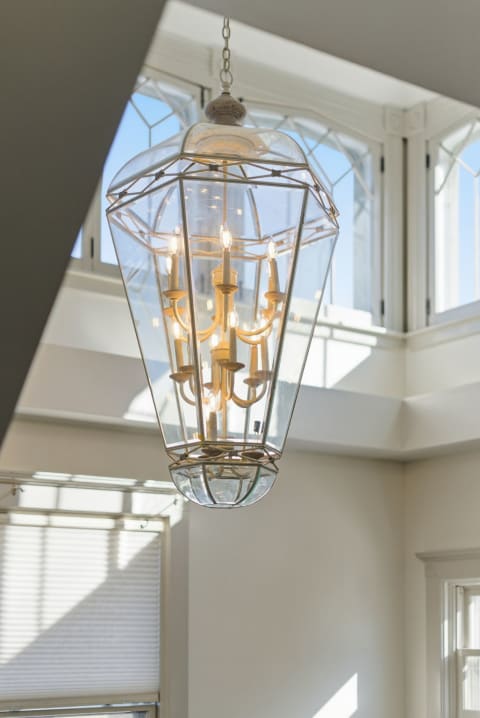 Elegant glass chandelier hanging in a sunlit room with large windows.