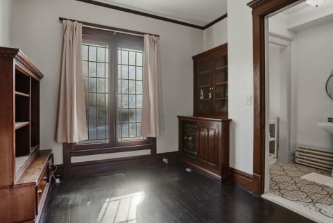 Small room off the kitchen showcasing dark wooden floors and large windows with beige curtains.
