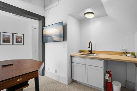Contemporary game room with a wall-mounted TV, gray cabinets, and wooden countertops.