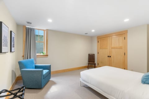 Minimalistic bedroom with a blue armchair, white bed, and wooden wardrobe