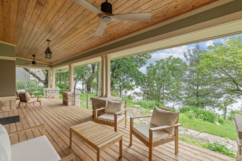 A serene lakeside porch featuring wooden flooring, comfortable chairs, and lush green surroundings.
