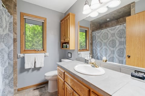 Interior view of a tidy bathroom featuring a shower, sink, and natural light from a window.