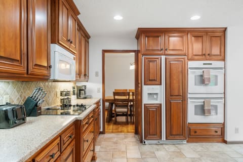 Interior view of a kitchen with wooden cabinets, modern appliances, and a dining area visible in the background.