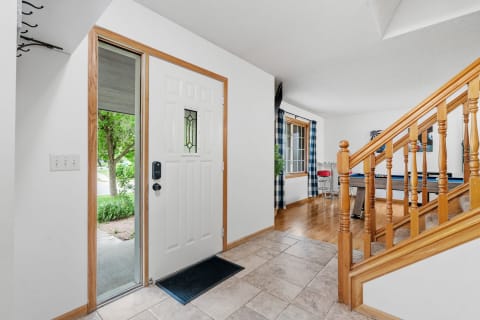 A welcoming entryway with a front door, staircase, and a seating area in soft natural light.