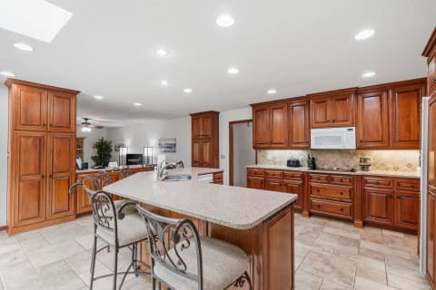 A spacious kitchen with granite island, wooden cabinets, and modern appliances.