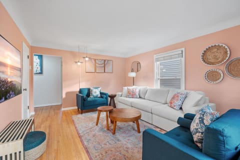 Modern living room with peach walls, white couch, teal chairs, and decorative elements.