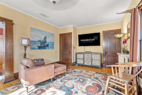 A living room with a brown leather sofa, a large nautical painting, and a TV displaying the Minnestay logo.