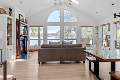 Spacious living room with large windows, gray sofa, and dining area featuring a wooden table.