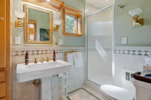 A stylish bathroom with a pedestal sink, ornate mirror, and shower enclosure.