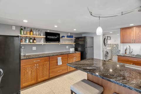 A contemporary kitchen with dark cabinets, granite countertop, and a mounted TV displaying a logo.