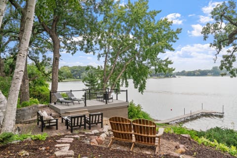 Lakeside view with wooden chairs and a dock.