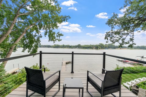 Balcony view overlooking a calm lake with black chairs and a wooden dock.