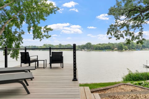 Deck with black wicker chairs beside a tranquil lake view under a blue sky.