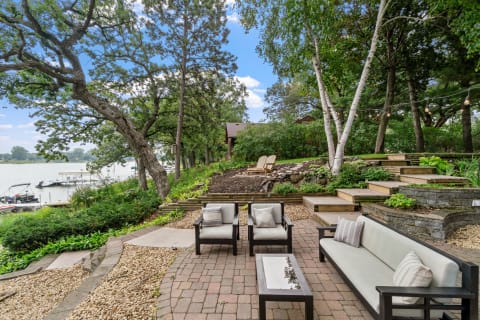 Lakeside patio area with outdoor seating, greenery, and view of the water.