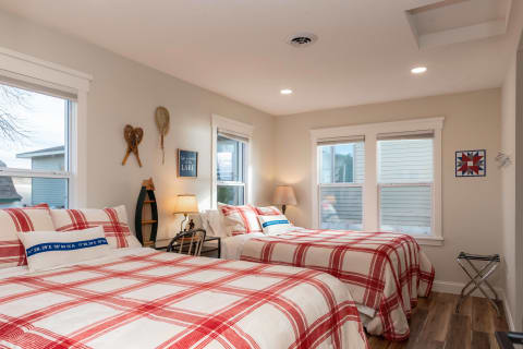 A light-filled bedroom featuring two beds with red plaid bedding and rustic decor.
