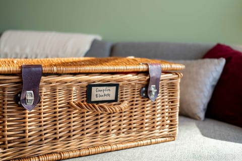 A wicker basket labeled 'Campfire Blankets' on a couch with colorful cushions.