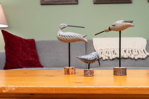 Three wooden bird sculptures on a table, with a cozy couch in the background.