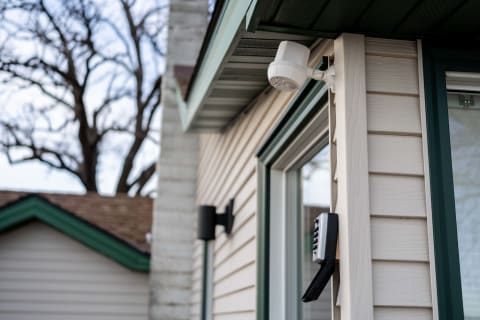 A close-up view of a house with a security camera on the wall and a combination lock box nearby.