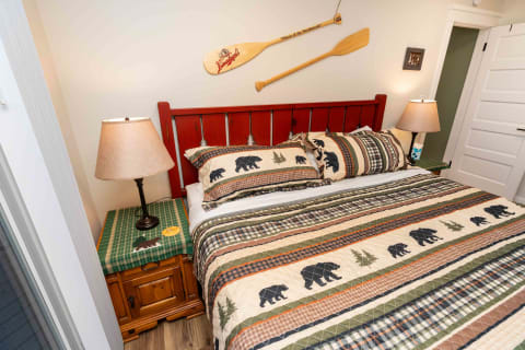 Cozy bedroom with a red wooden headboard, bear-patterned quilt, and rustic decor.