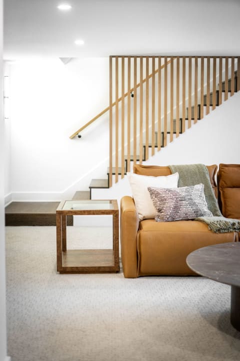 Stylish basement living area featuring a leather sofa and wooden staircase.